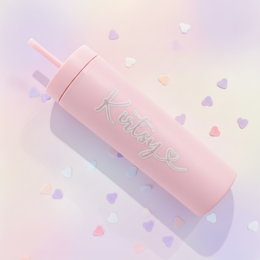 Personalised pink cold cup with custom name, handmade in UK, lying flat on dreamy pastel gradient background with scattered heart confetti